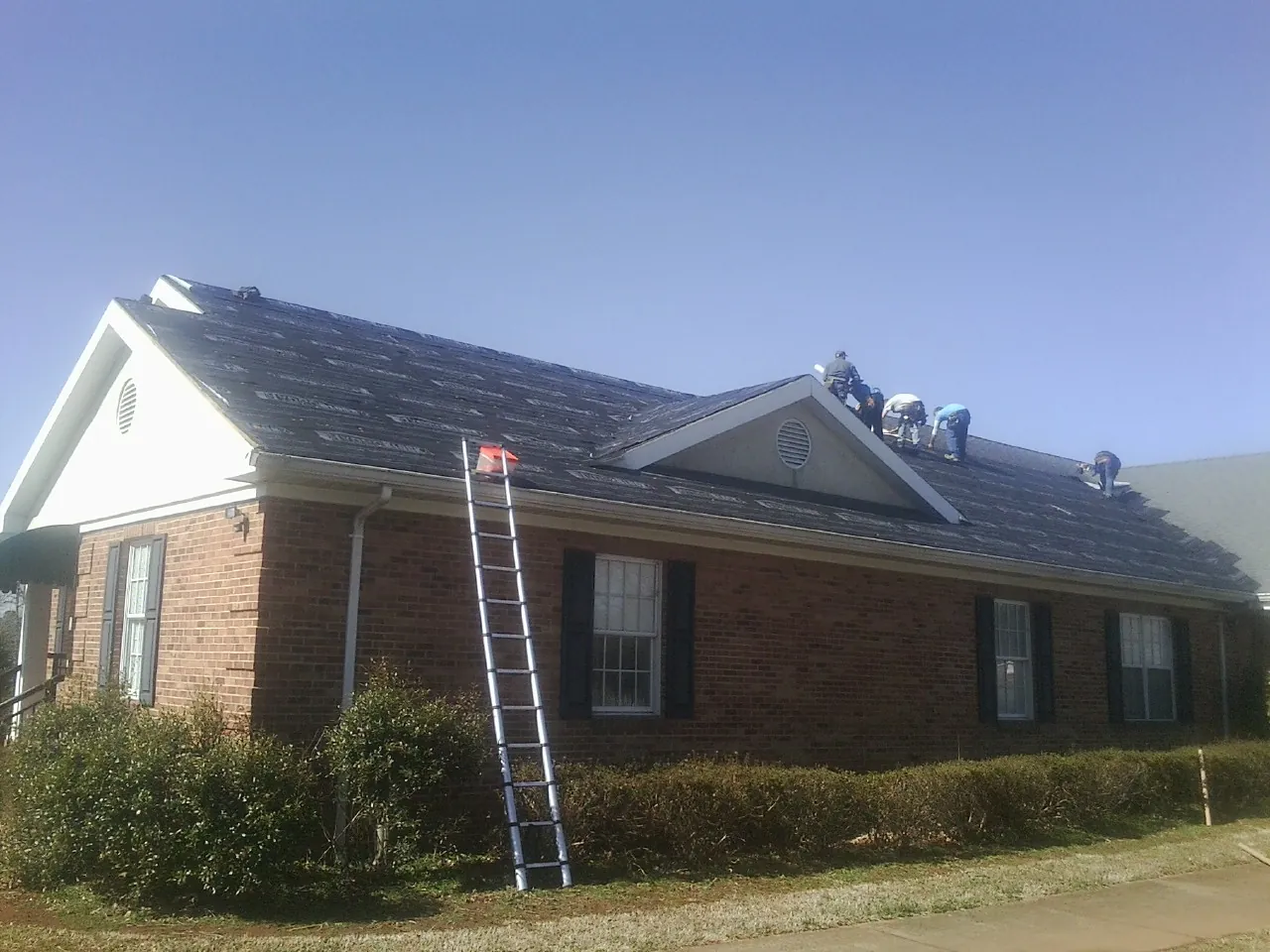 Crew tearing shingles off a brick ranch roof with a ladder set — Emergency Roof Repair work by our crew in Bloomingdale