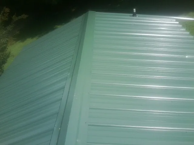 New green metal panels meeting at the ridge of a roof — Flat Roof Repair work by our crew in Bloomingdale