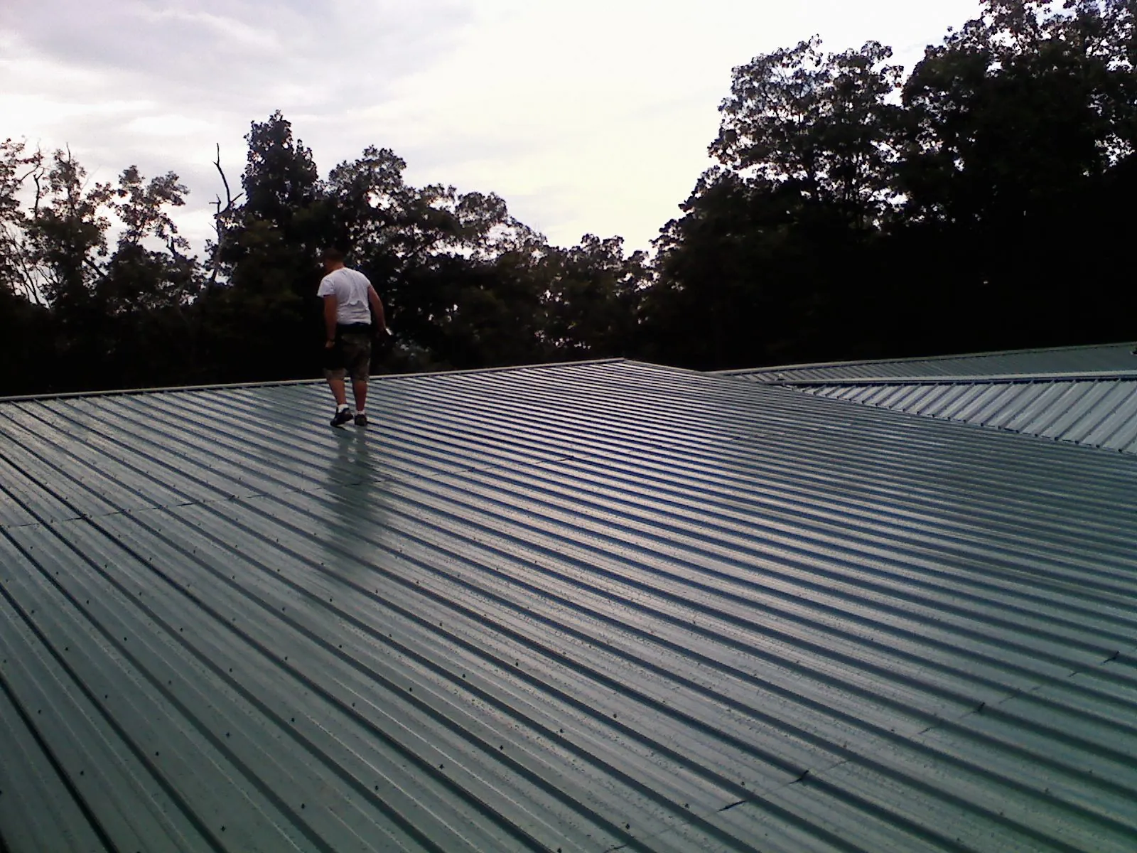 Roofer walking a wide expanse of new green metal roofing in Bloomingdale