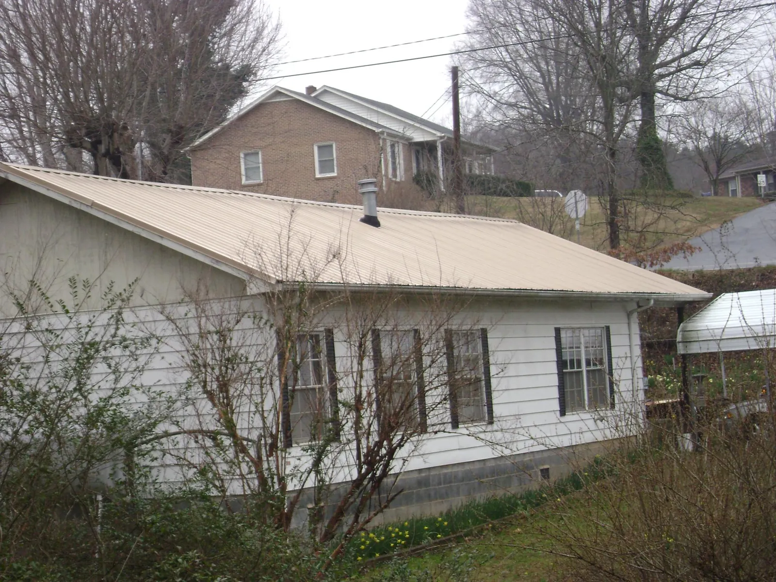 Tan metal roof on a white sided house set into a hillside — Commercial Roofing by Roofing Brothers in Bloomingdale